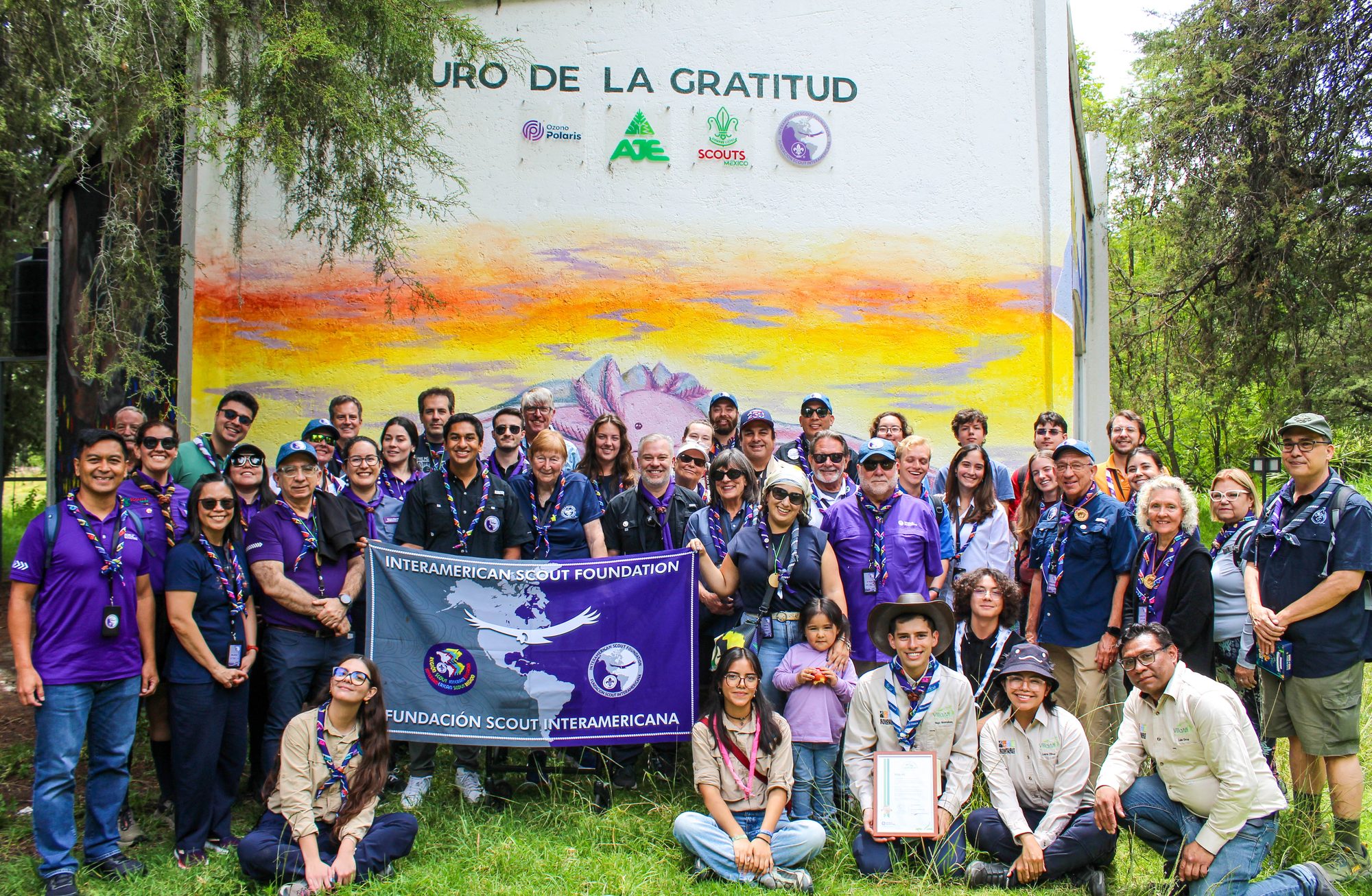 Participants of the Condor Experience 2026 holding the Interamerican Scout Foundation banner in front of the Muro de la Gratitud mural at Villa Atl